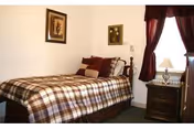 A cozy bedroom with plaid quilt, dark wood furniture, and burgundy curtains.