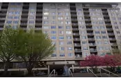 Tall multi-story senior living facility building with trees and a ramp at the entrance.