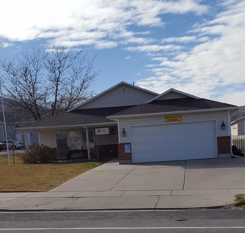 Single-story assisted living facility with beige siding, attached garage, and entrance sign.