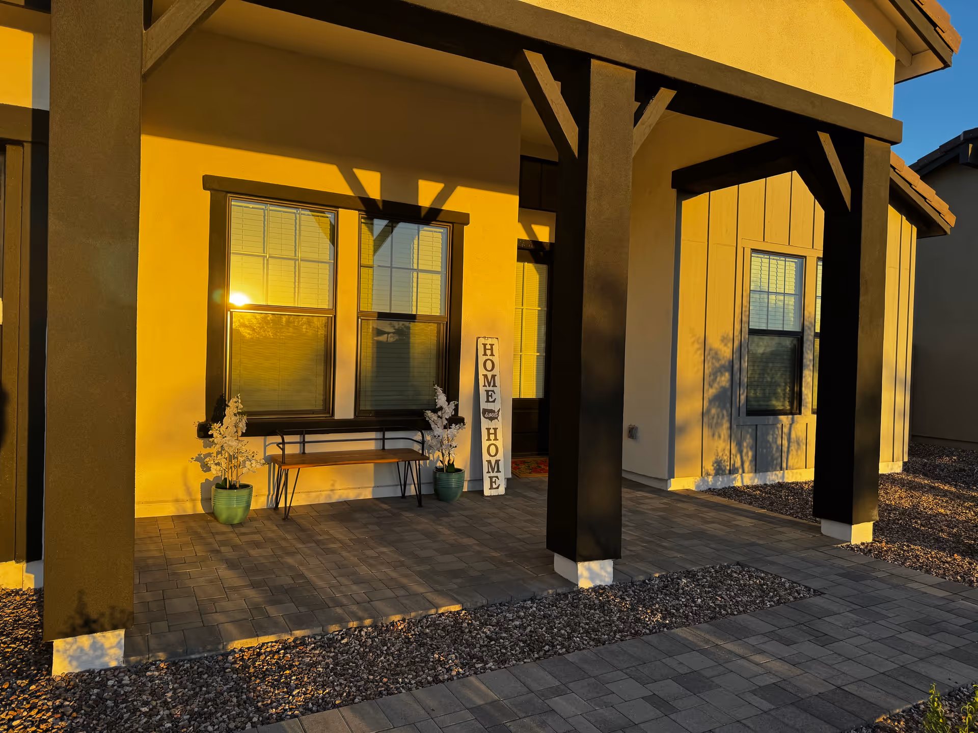 Yellow building exterior with dark columns, front porch, bench, and potted plants.