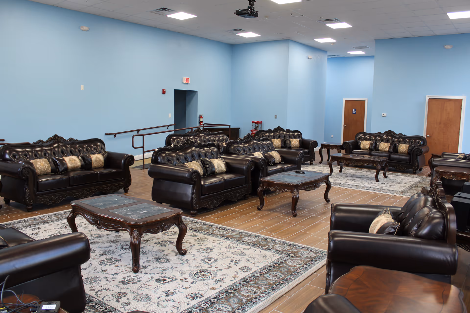 A spacious lounge with black leather sofas, wooden coffee tables, area rugs, and blue walls.