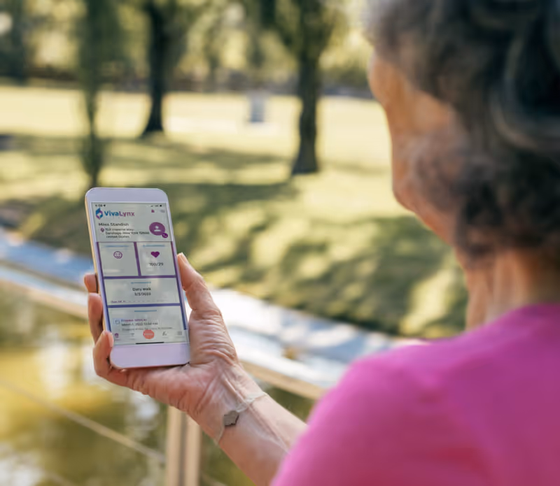 Older adult's hand holds a smartphone outdoors beside a park pond.