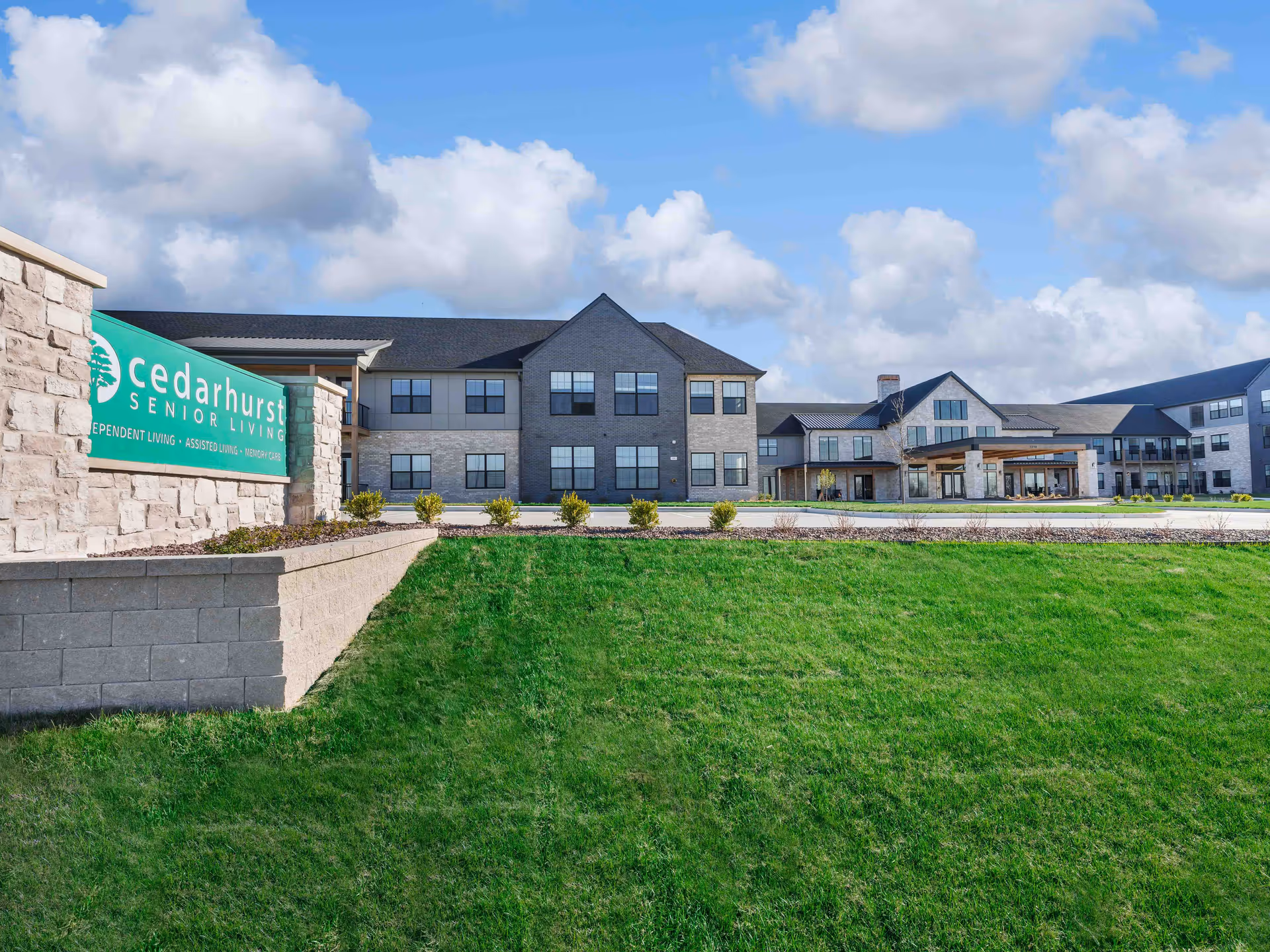 Front exterior view of the Cedarhurst Senior Living building with a stone sign, green lawn, and main entrance.