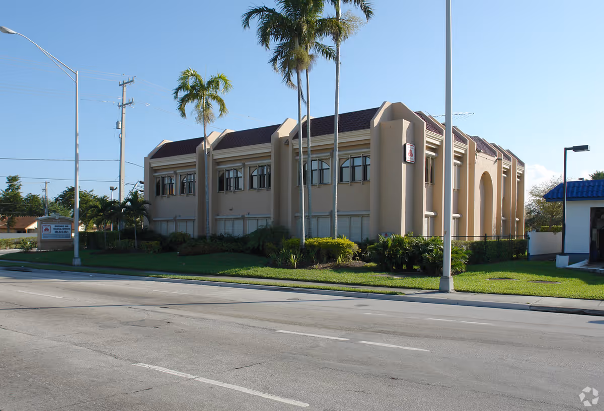 Exterior view of a beige senior living facility with palm trees along the street