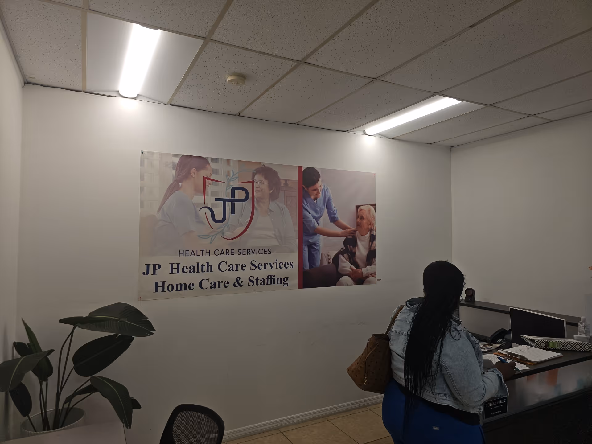 Reception area with a JP Health Care Services poster and a seated visitor.