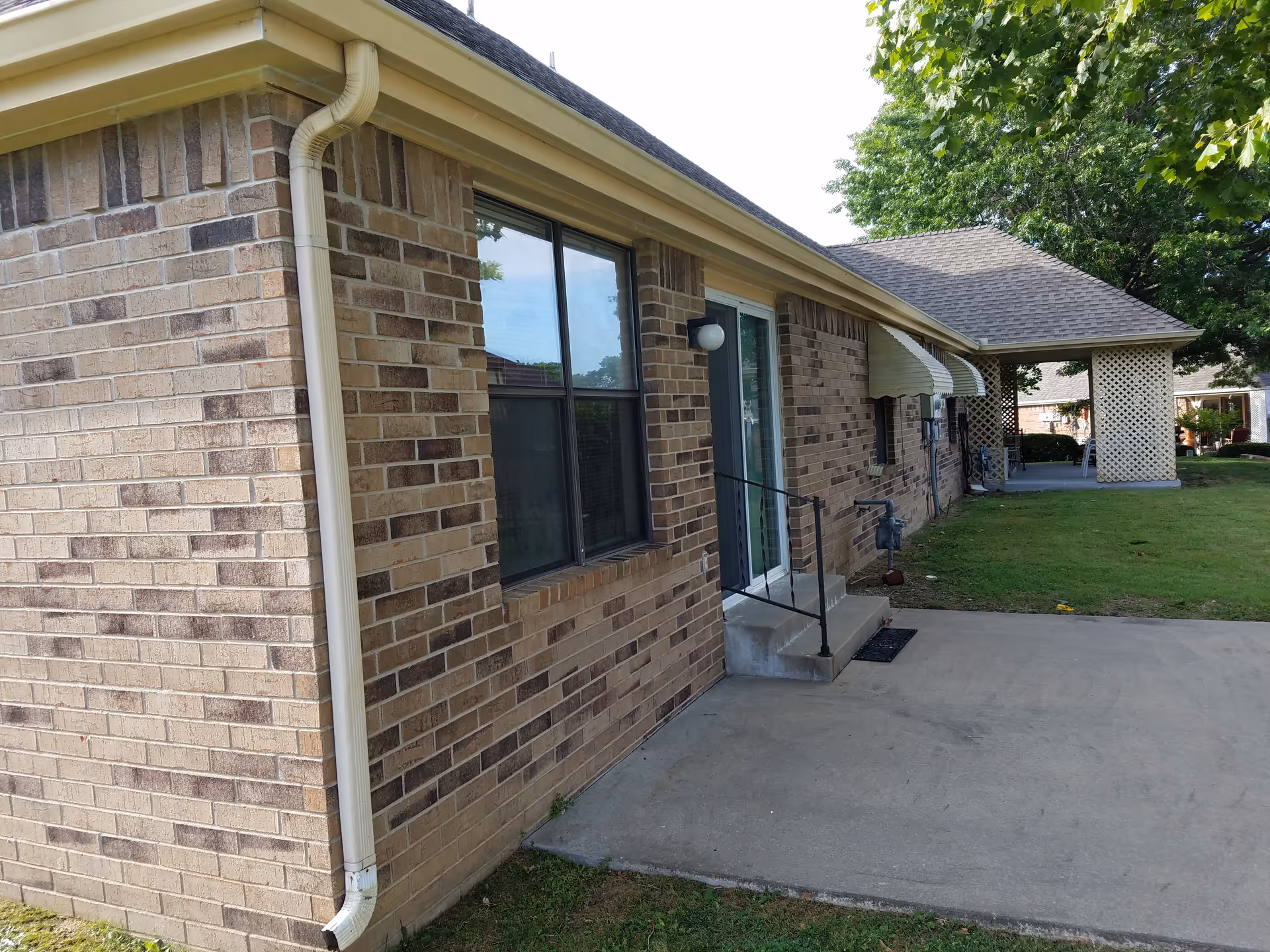 Brick exterior of a senior living facility with windows, steps, sidewalk, and lawn.