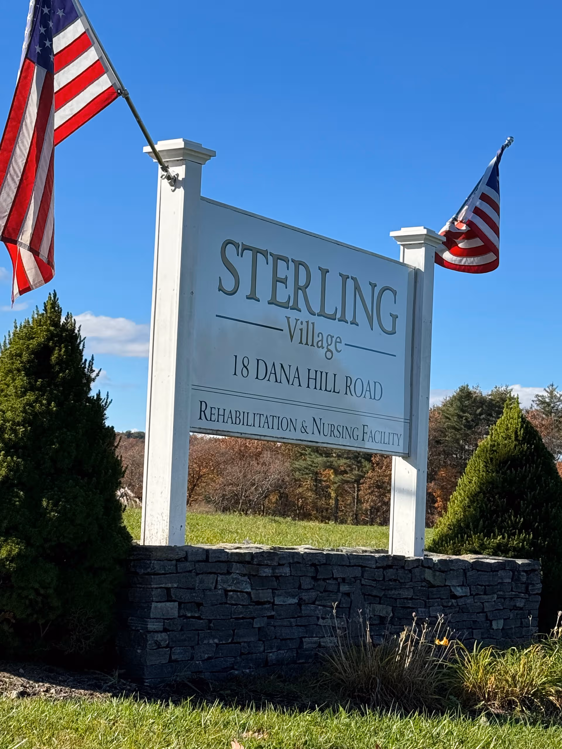 A large white Sterling Village sign on a stone base with American flags.