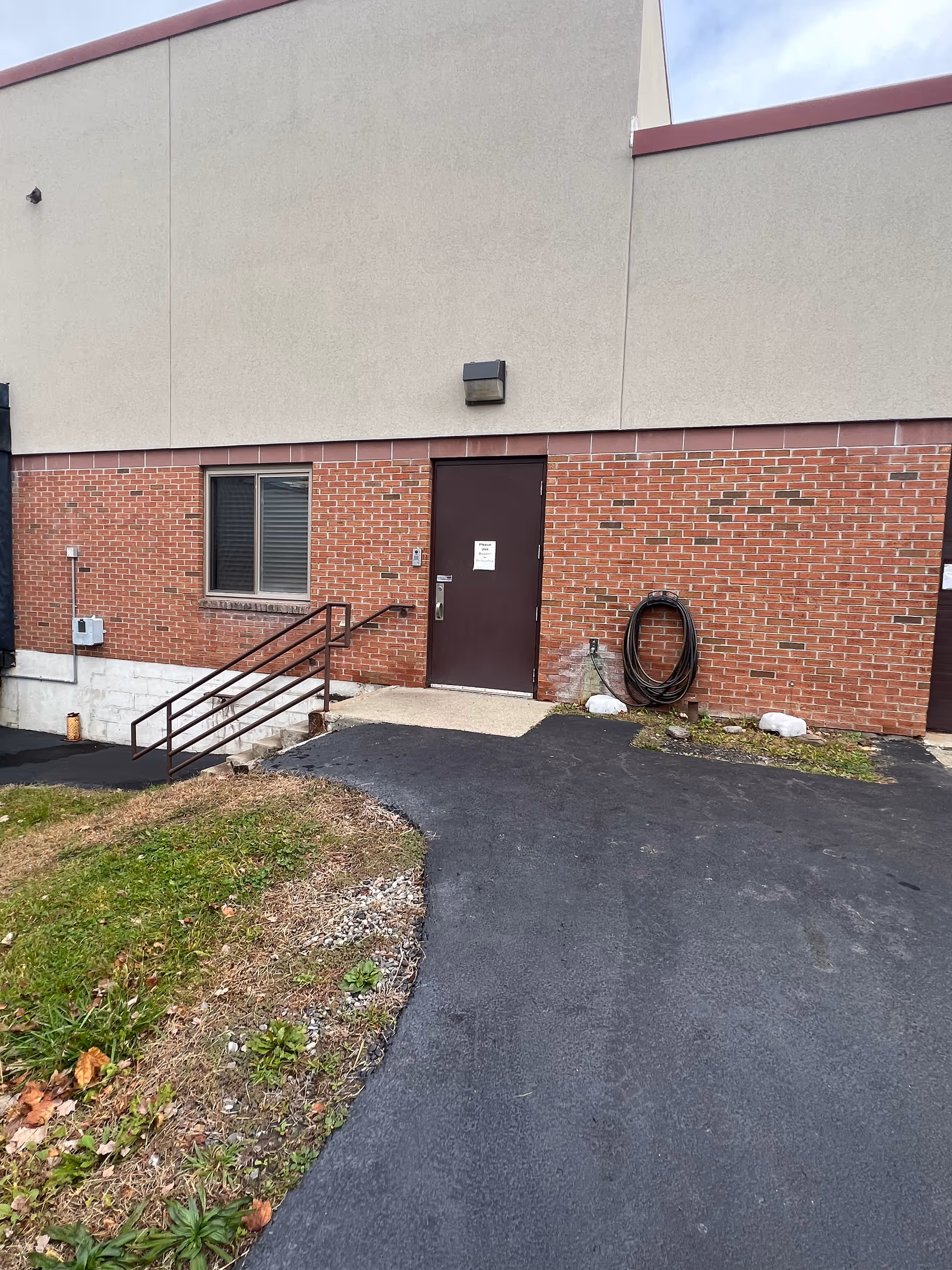 Exterior view of a brick facility entrance with stairs, ramp, and a coiled hose.