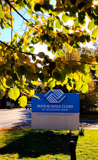 Sunlit outdoor scene featuring a Boys and Girls Clubs sign among autumn leaves.