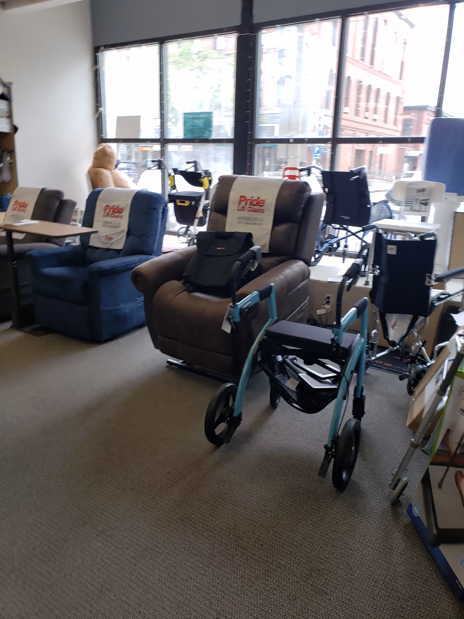 Indoor showroom with recliner chairs, a wheelchair, walkers, and large storefront windows.