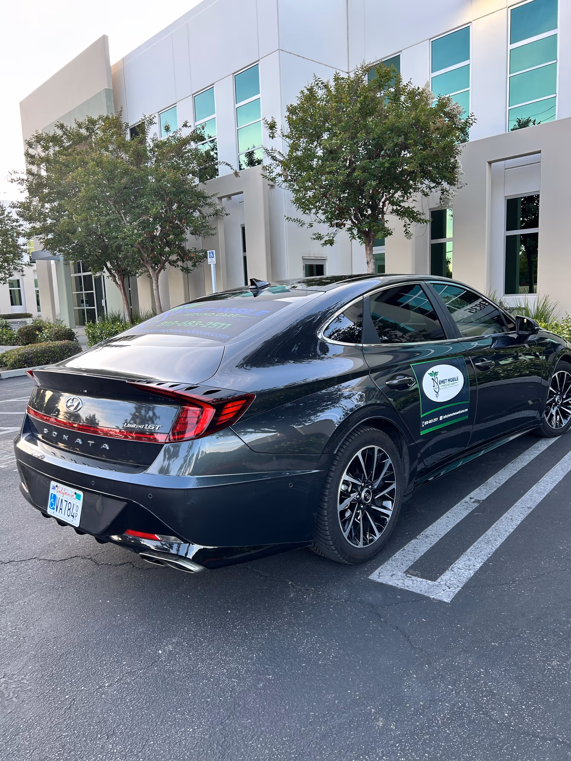 Dark sedan with Emet Mobile Wound Care sticker parked in a lot by a modern building.