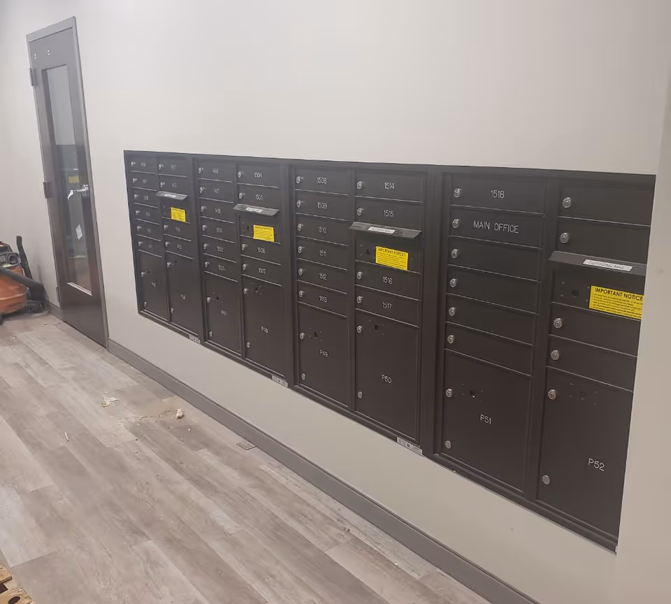 Interior hallway with row of black mailboxes along a pale wall and glass door.