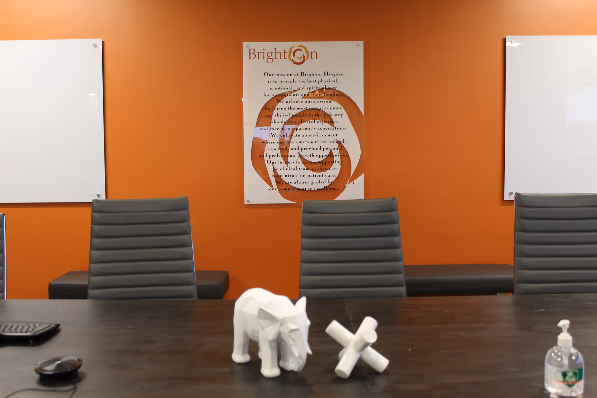 An orange-walled conference room with a Brighton Hospice poster, whiteboards, and modern chairs.