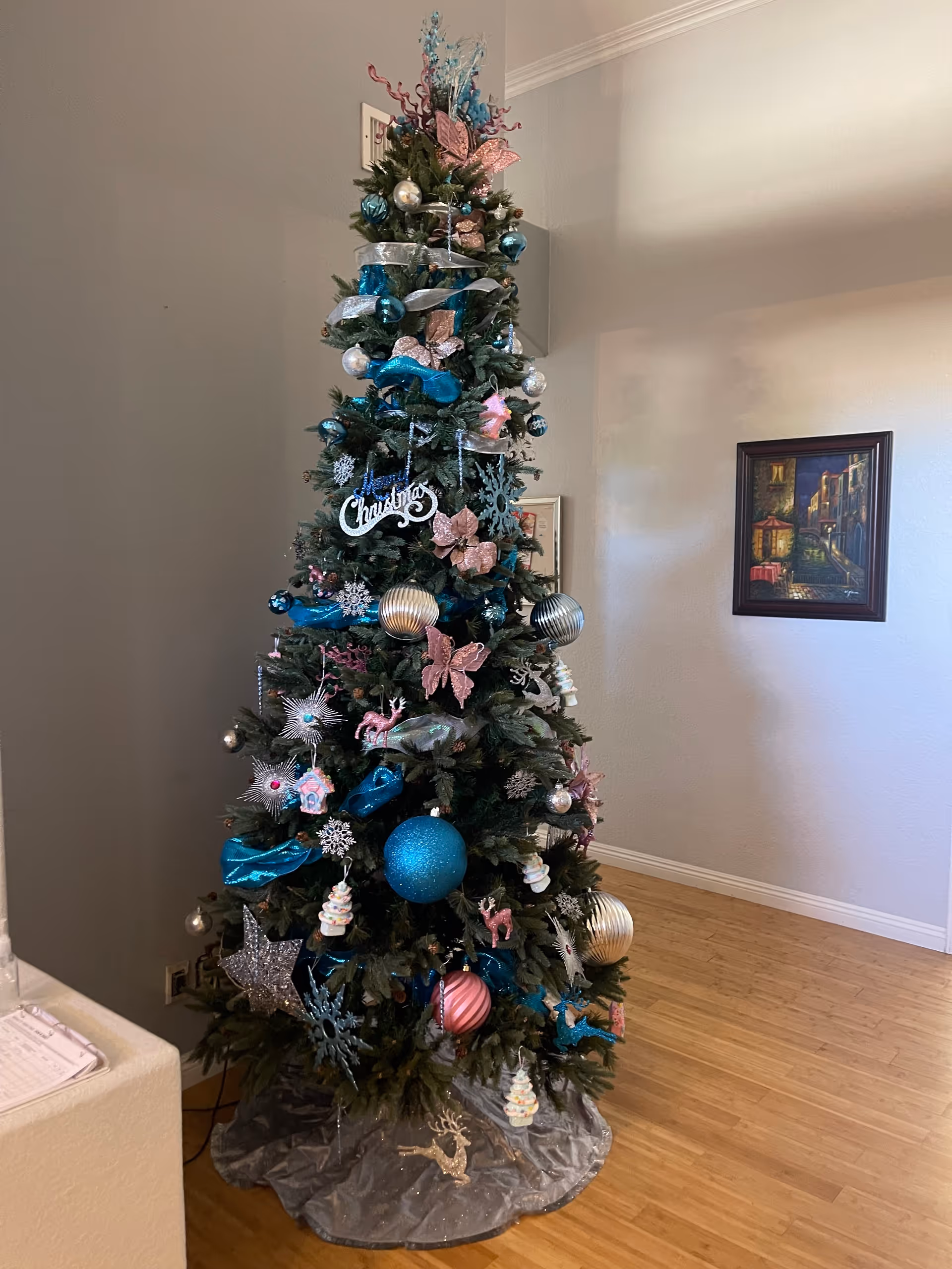 Decorated Christmas tree with blue, pink, and silver ornaments in a hardwood-floored interior room.