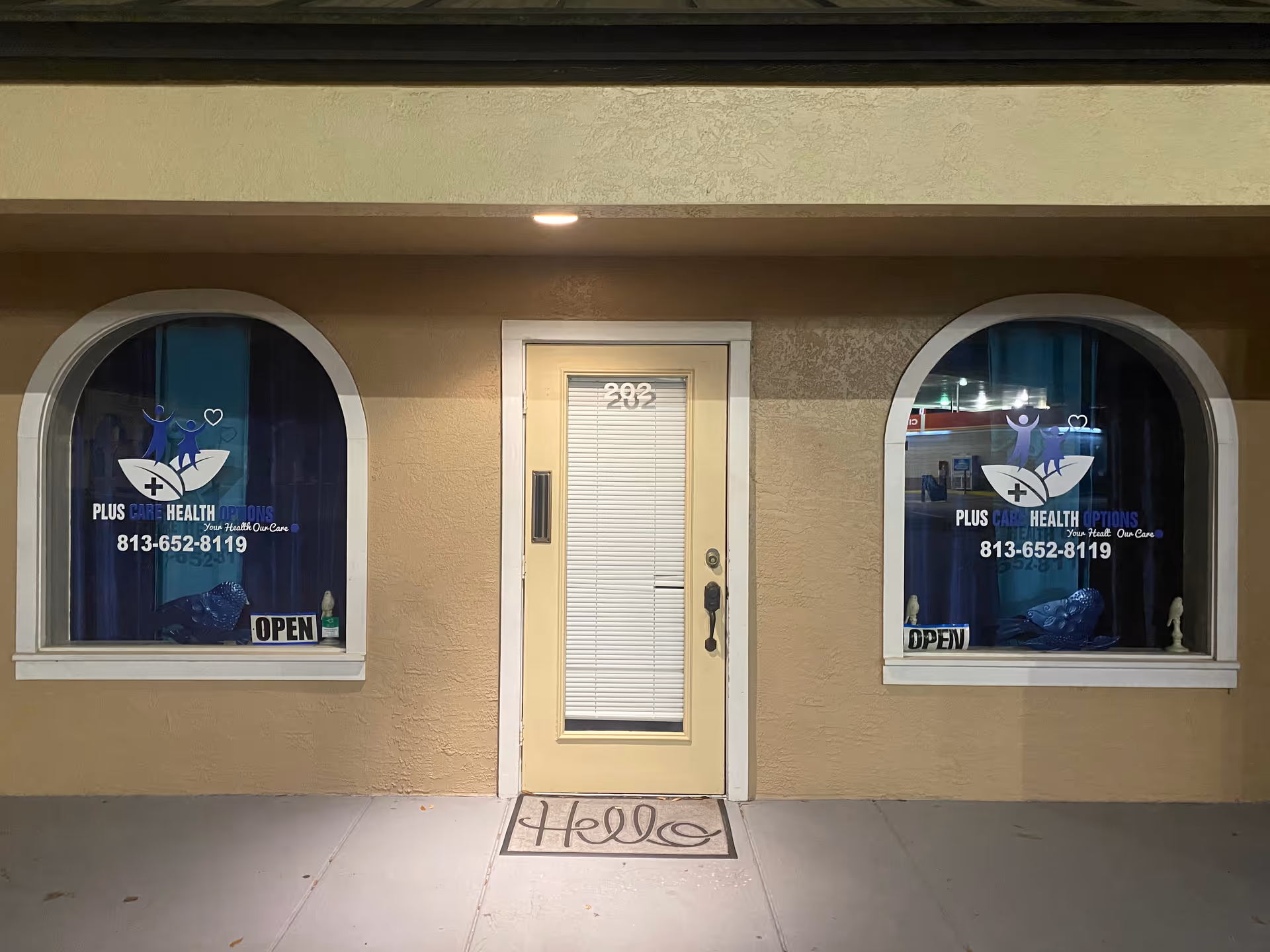 Front entrance of Plus Care Health Options with arched windows and an 'OPEN' sign.