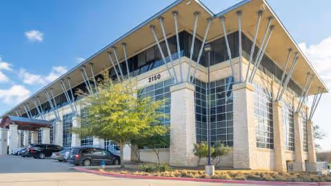 1Mission Home Care building with expansive glass walls, distinctive support columns, and a parking lot.