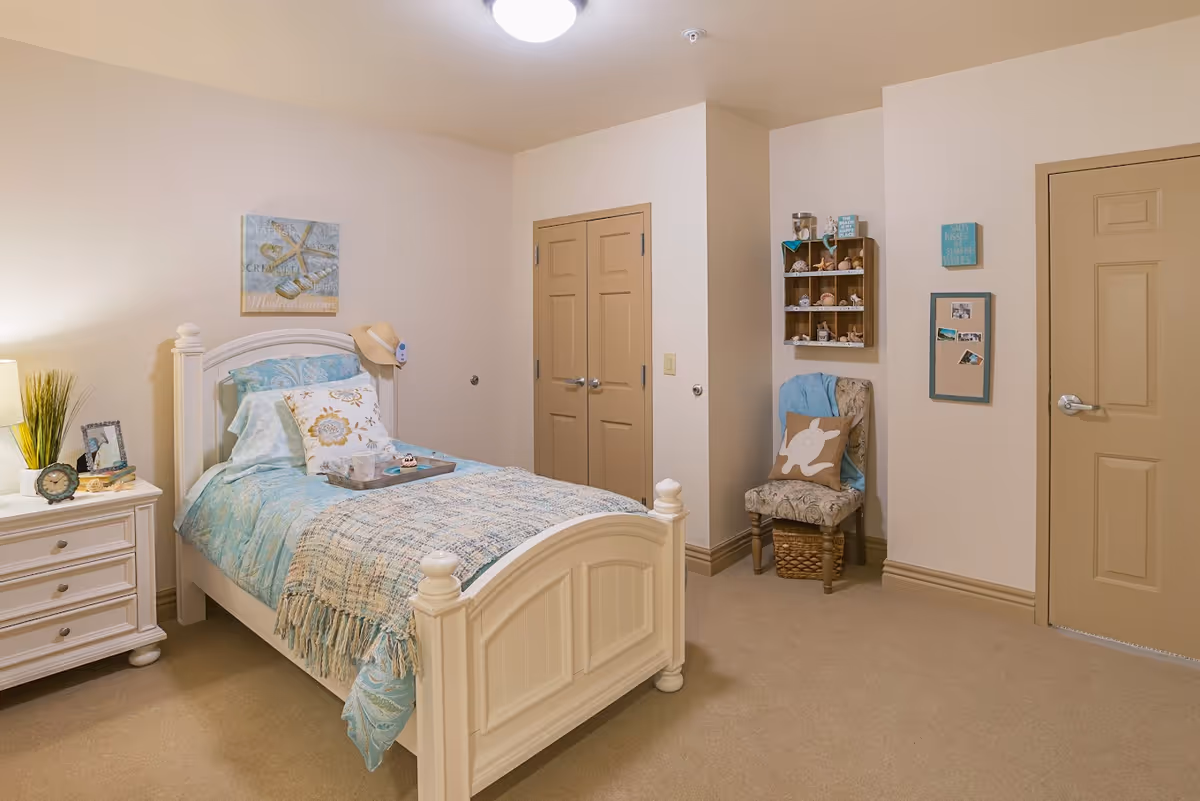 White bed with blue bedding and cozy décor in a senior living bedroom.