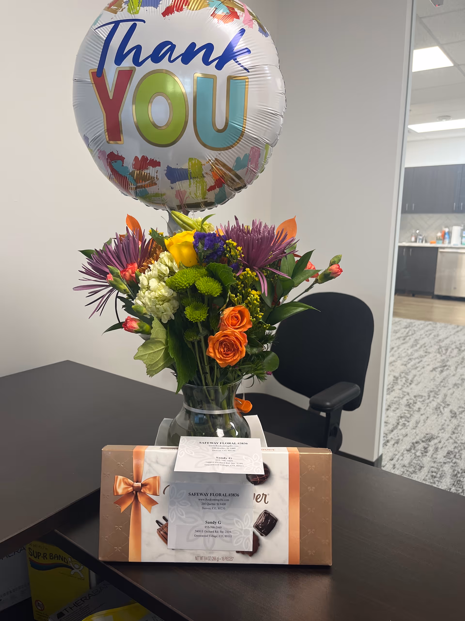 Inside a reception area, a vase of flowers and a thank you balloon on a desk.