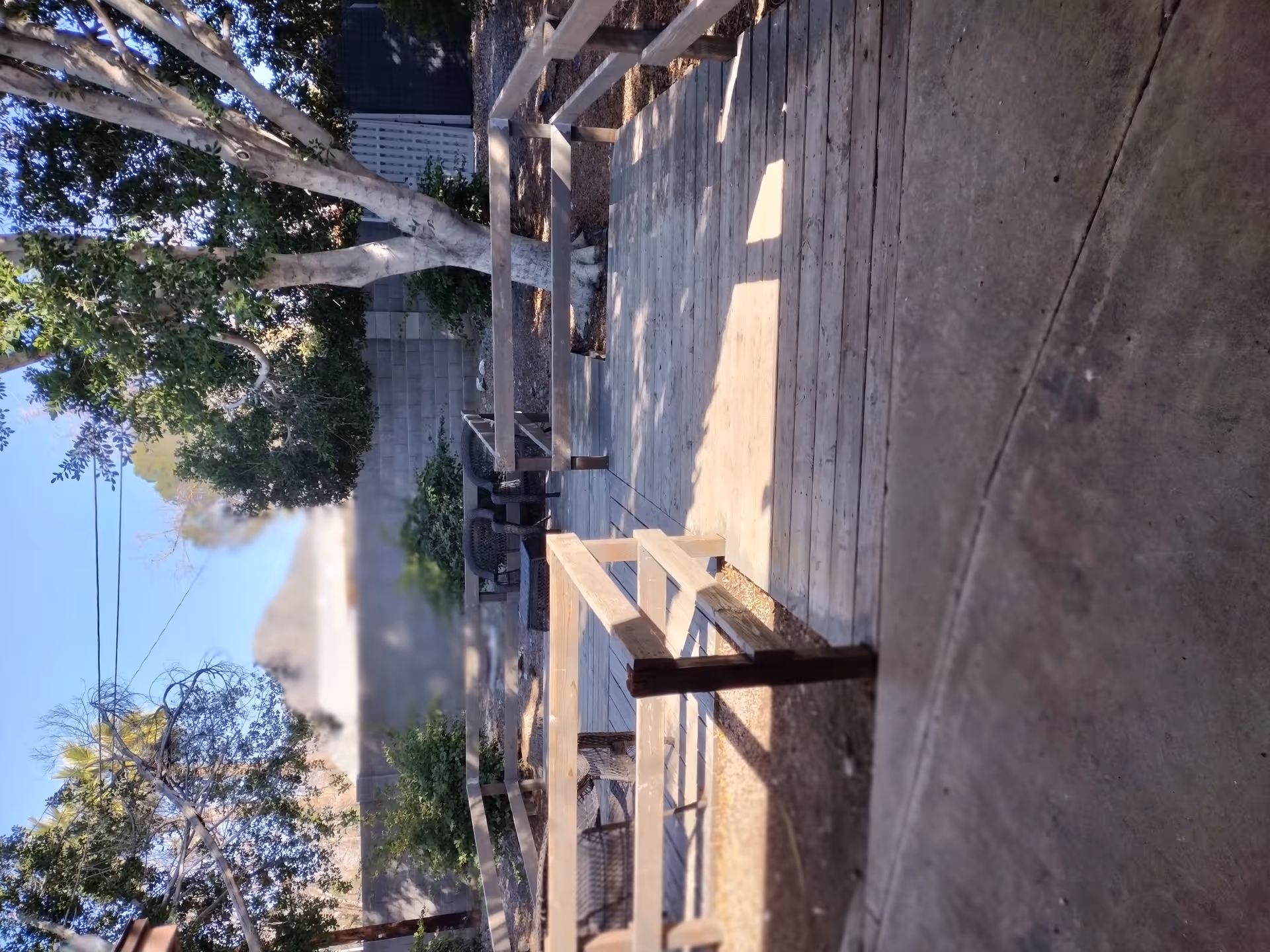 Outdoor wooden patio with benches, a table, and surrounding trees.