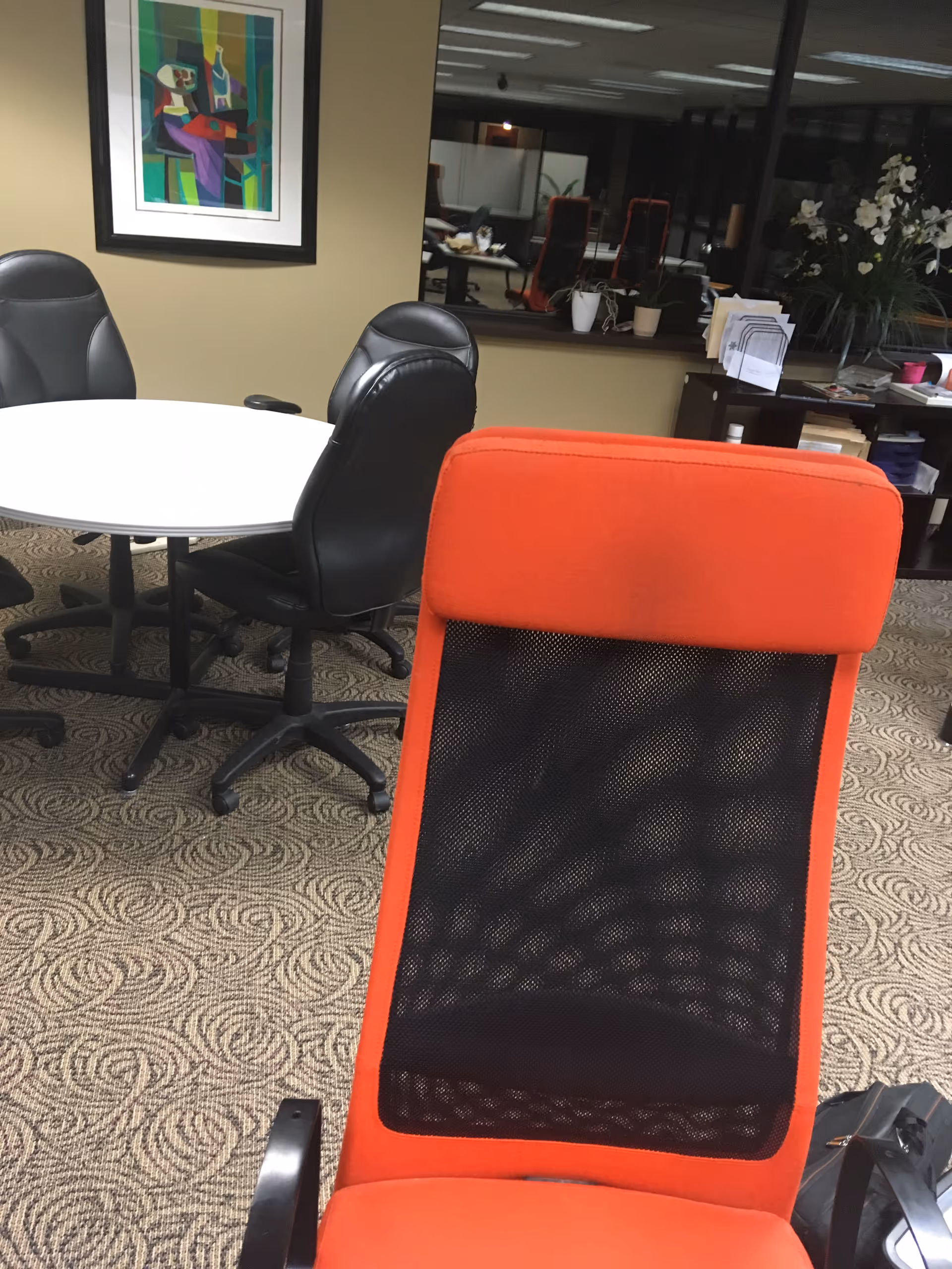Red mesh-back chair in foreground; round table and black chairs in a lounge area.