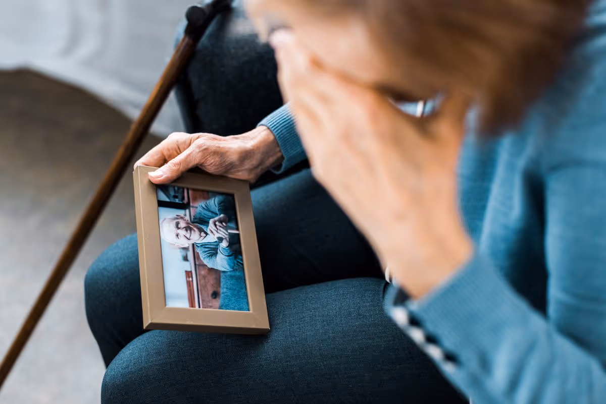 A person sits indoors, holding a photo frame showing an elderly smiling woman.