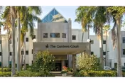 Front view of a light-colored senior living building with palm trees and a sign.
