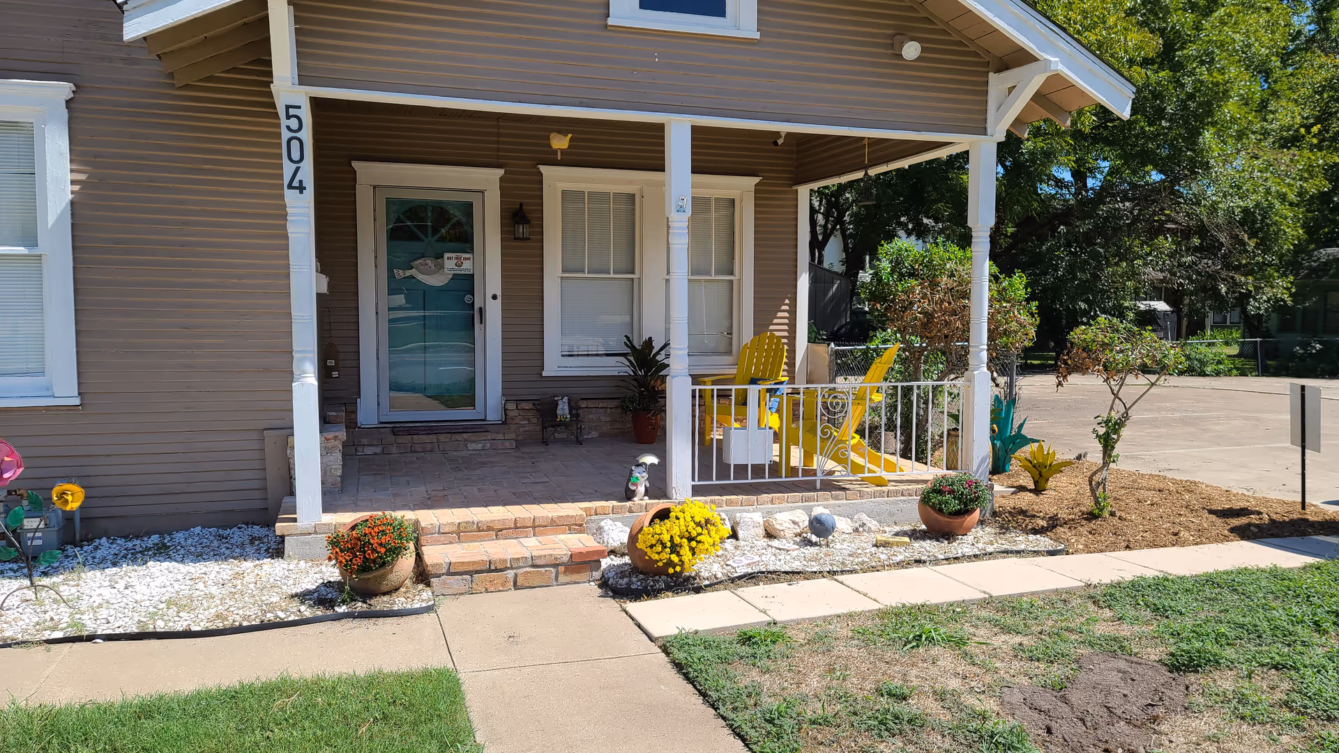 Front porch of a brown house with yellow chairs and potted plants.