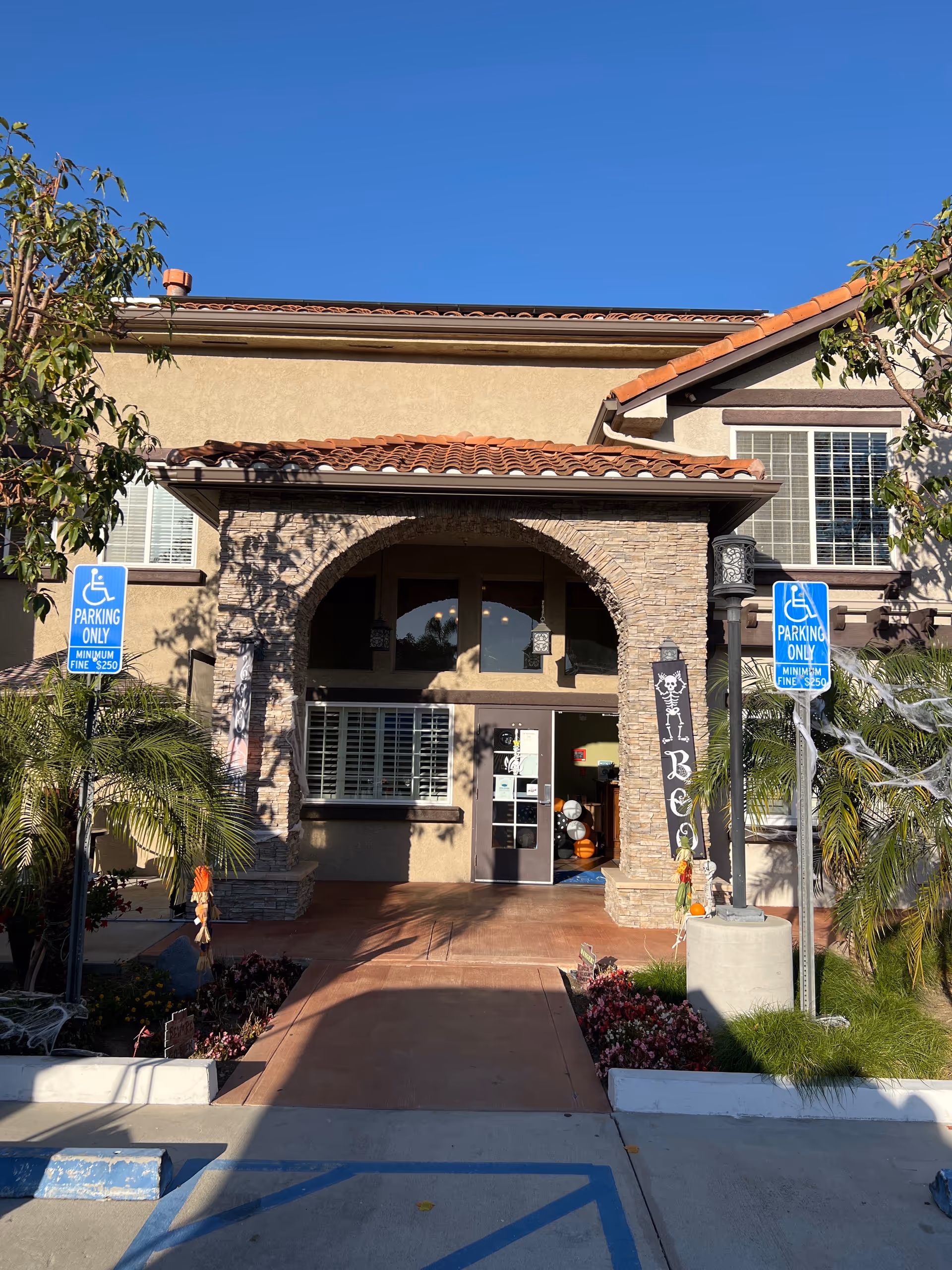 Exterior view of Pacifica Senior Living South Coast building entrance with archway and parking signs.