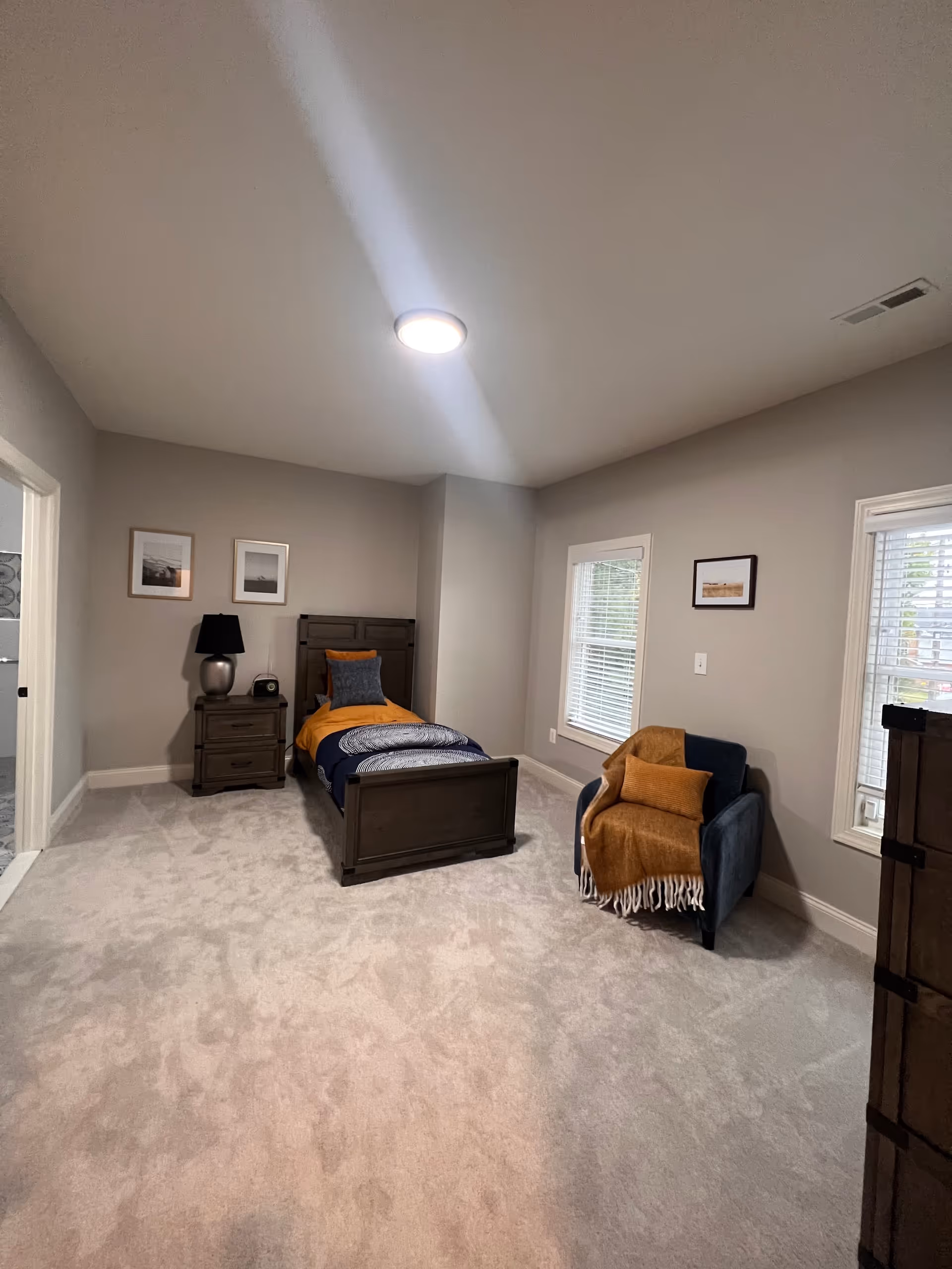 A spacious bedroom featuring a single bed, nightstand, chair, and two windows.