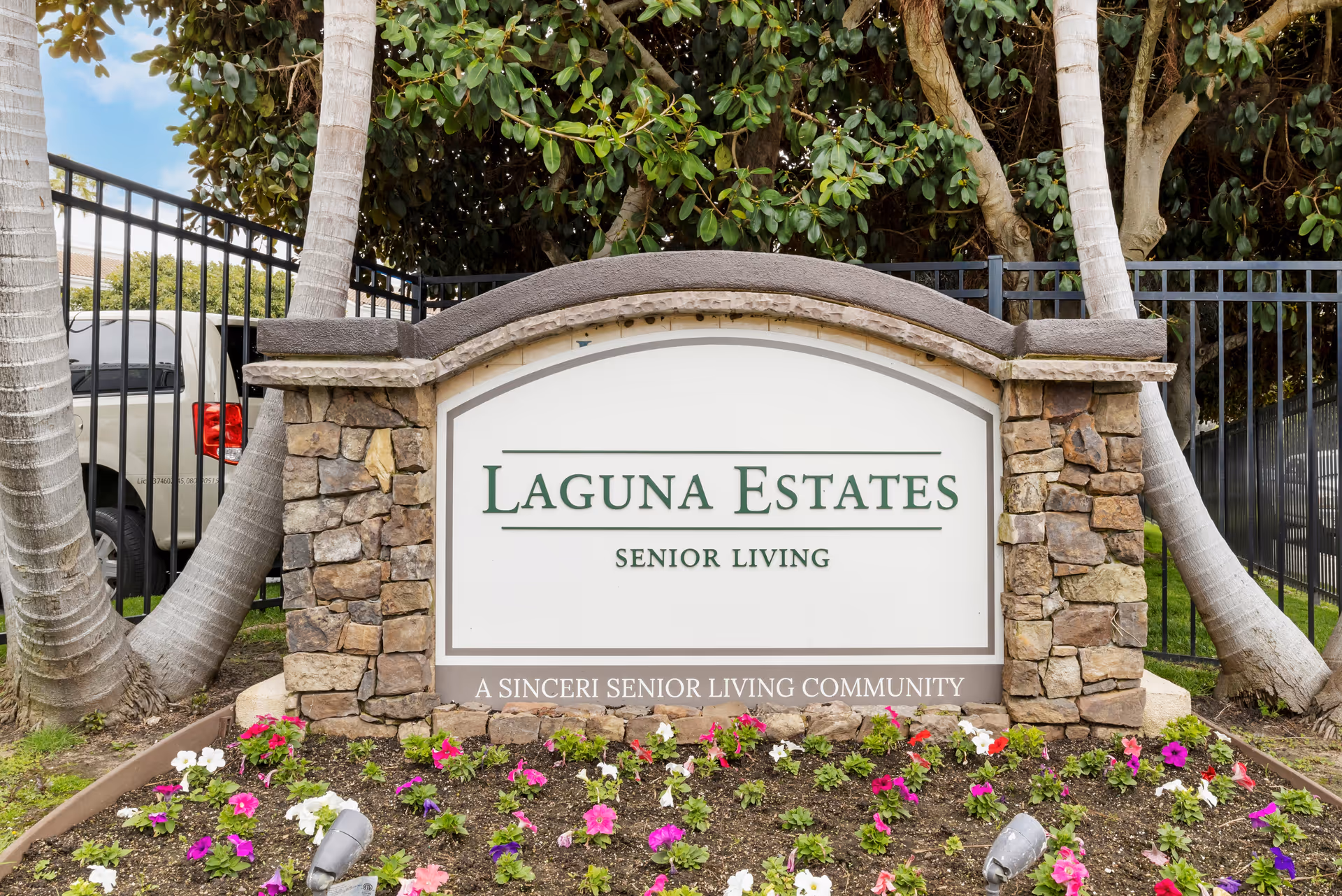 Laguna Estates sign for senior living framed by stone pillars and blooming flowers.