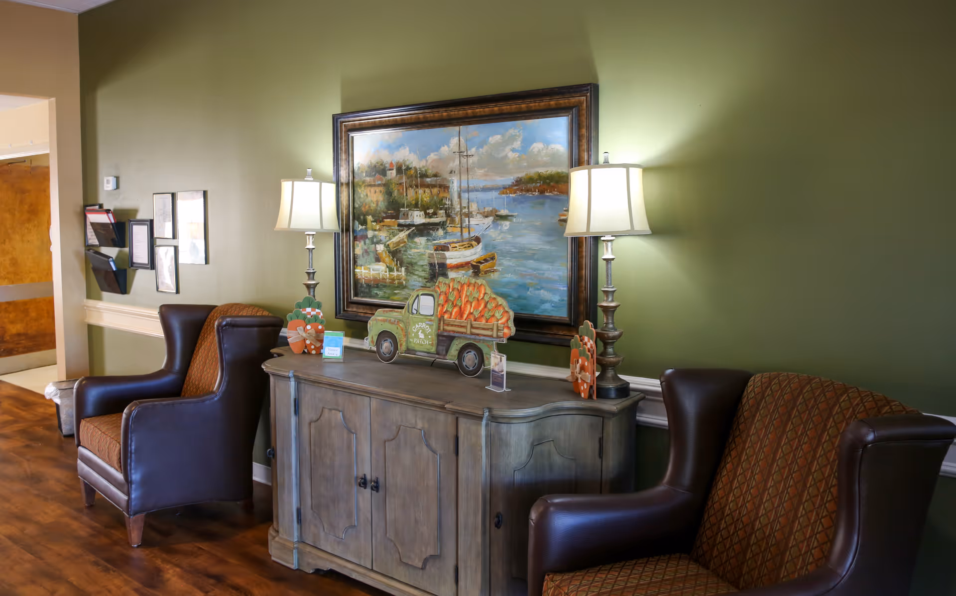 Green-walled lounge area with a wooden console, two leather chairs, and a framed harbor scene.