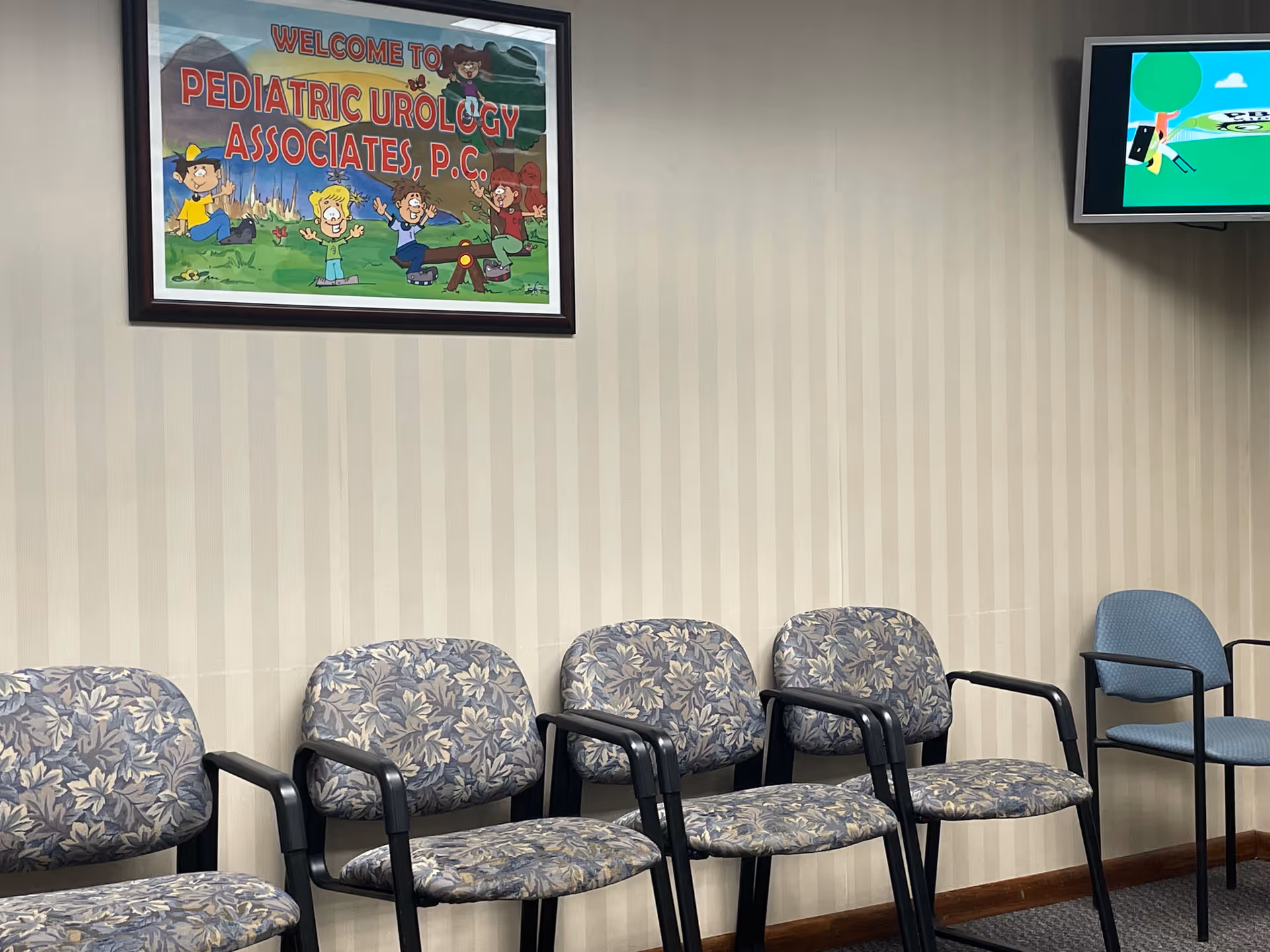 Waiting area with six patterned chairs against a striped wall and a framed pediatric urology sign.