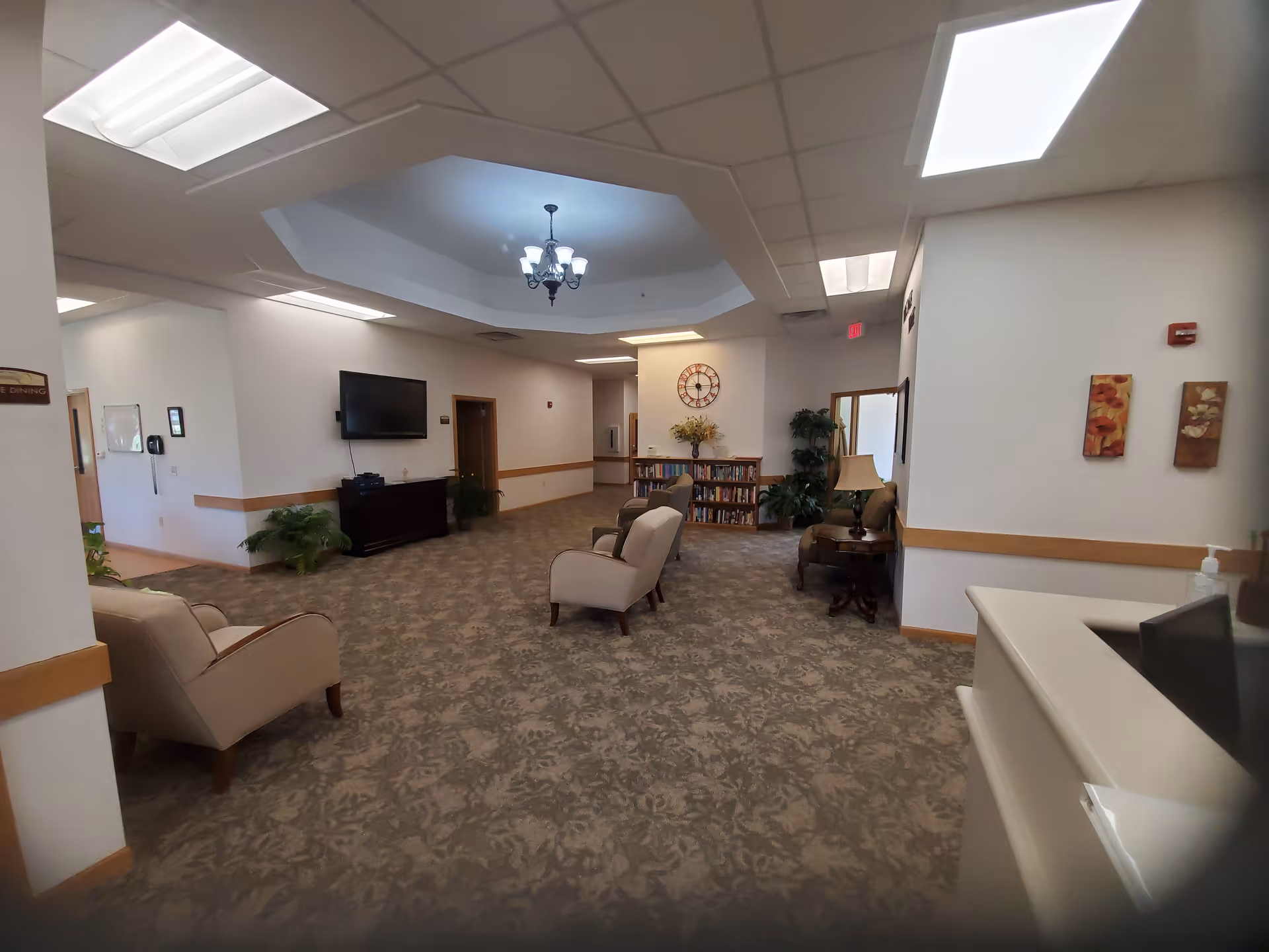 Senior living lounge with chairs, a TV, chandelier, and bookshelves.