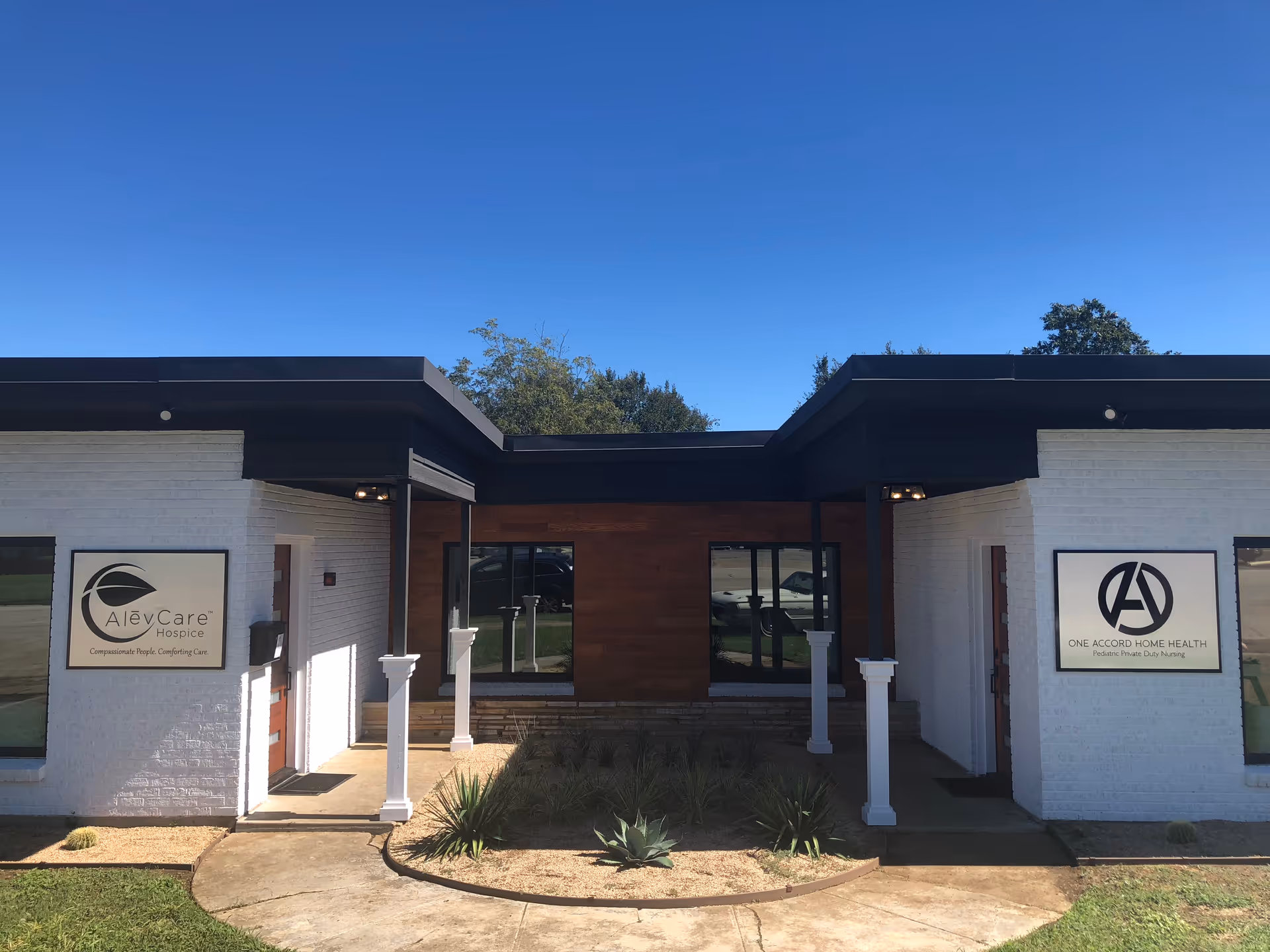 Modern hospice building entrance on a white brick facade with signs and blue sky.