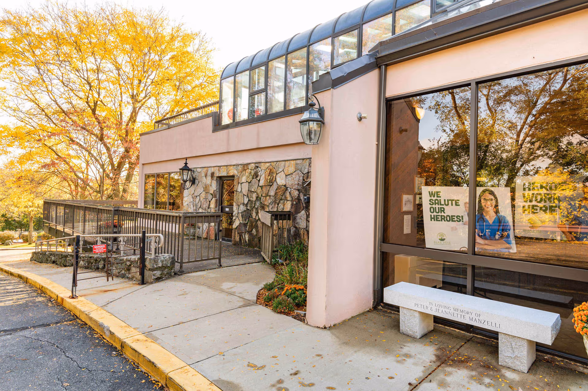 Exterior view of Bear Hill Nursing Center entrance with glass windows and autumn trees.