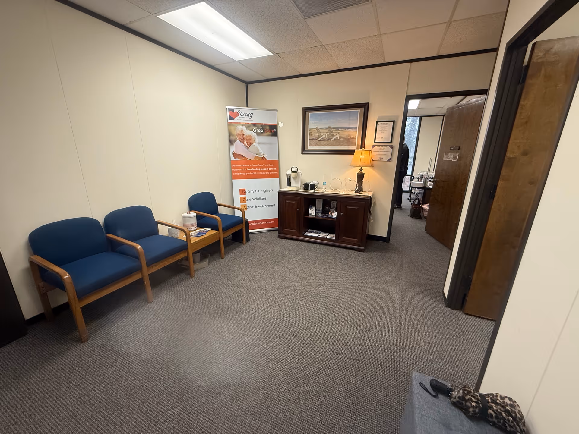 A small waiting area with blue chairs, a banner, and a wooden cabinet.
