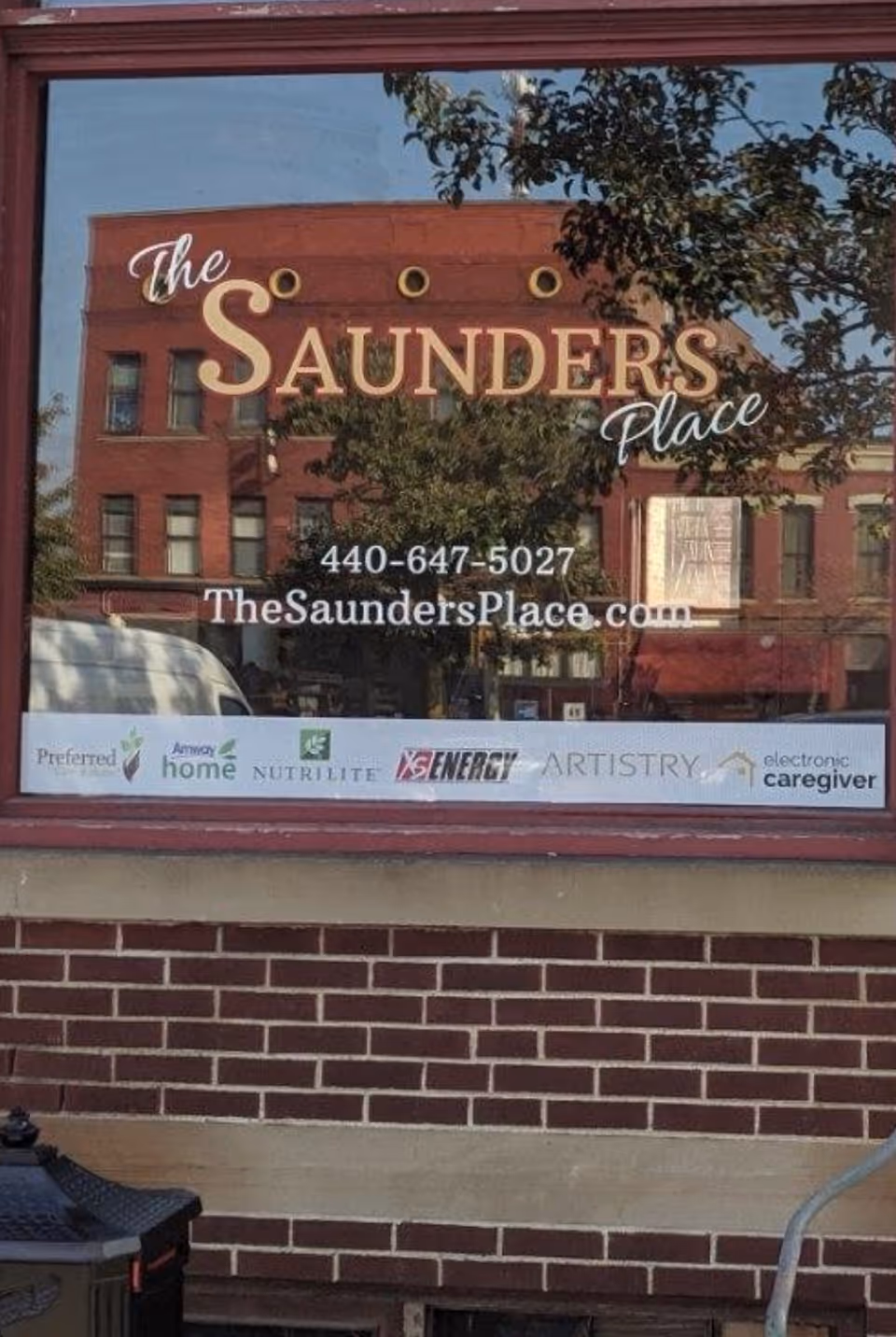 Glass window signage for The Saunders Place on a brick building with logos.