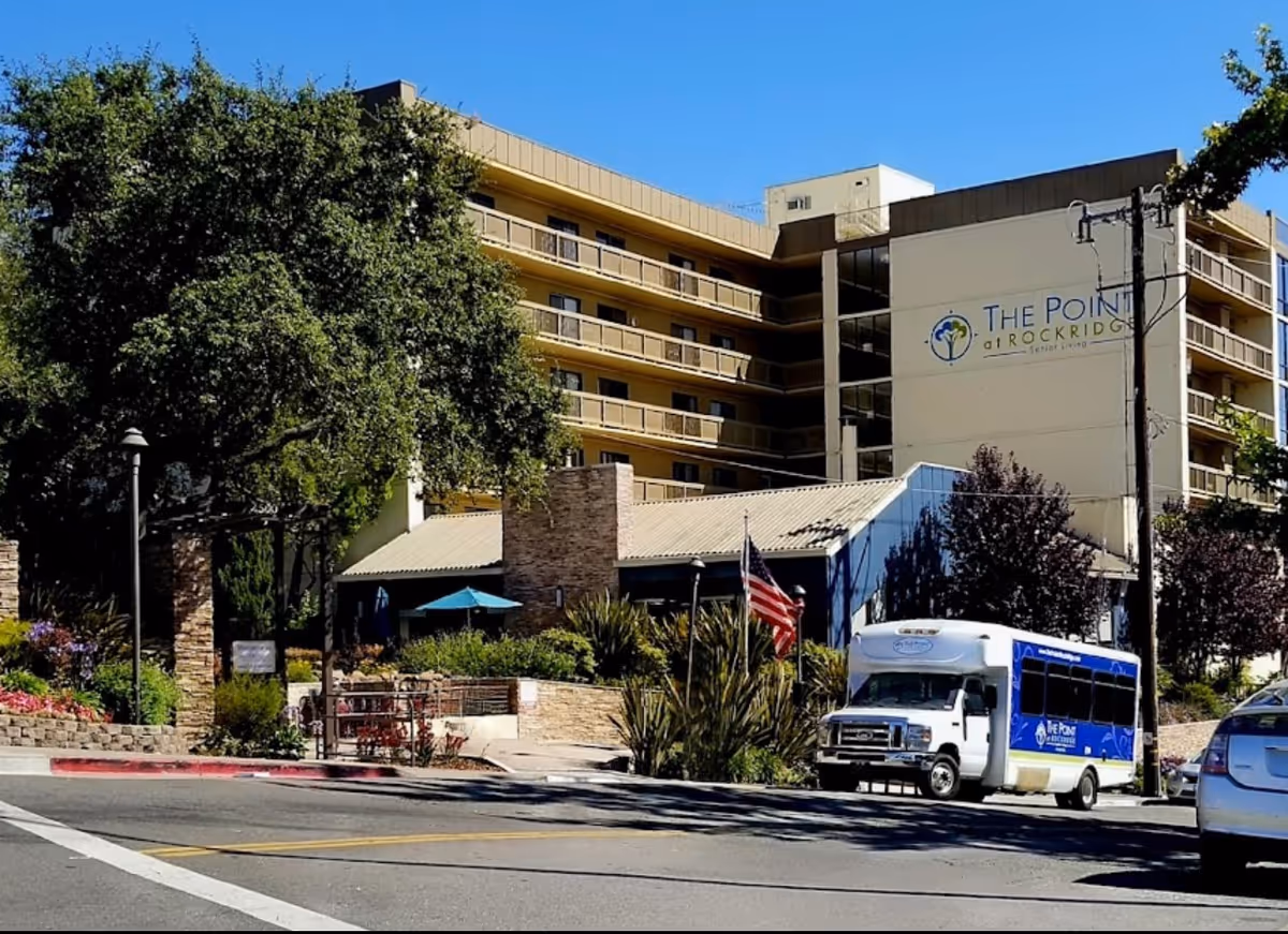 Exterior view of The Point At Rockridge Senior Living building with white shuttle bus in front.