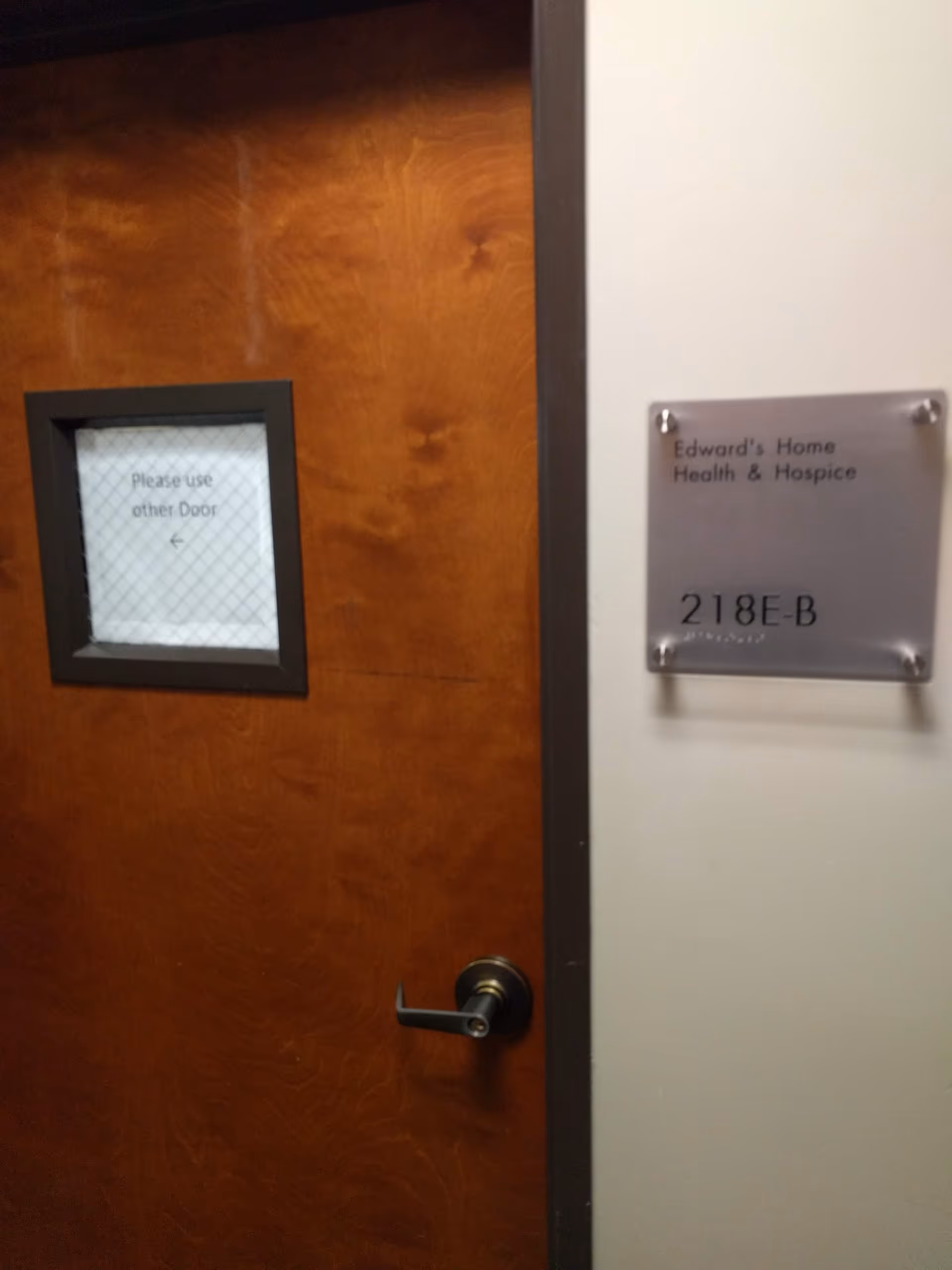 Wooden interior door with a window and a wall plaque for Edwards Home Health Hospice.