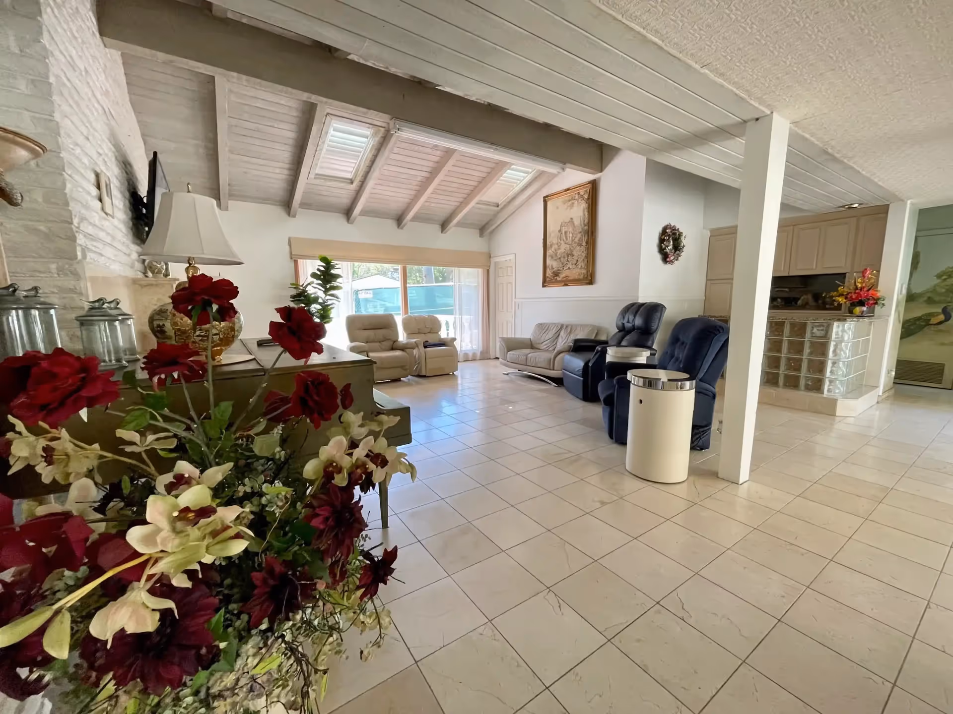 Spacious PVE Manor lounge with tiled floor, armchairs, sofas, and flowering decor.