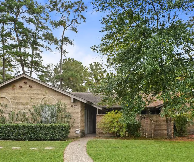 Brick cottage-style senior living building with a walkway and surrounding trees.