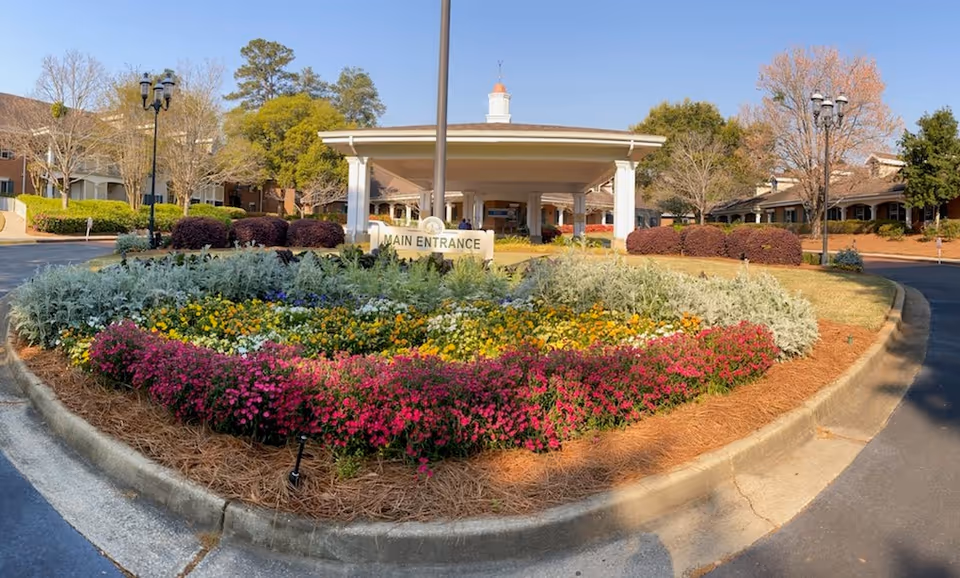 Front entrance of Brandon Wilde senior living facility with a circular, colorful flower bed and canopy.