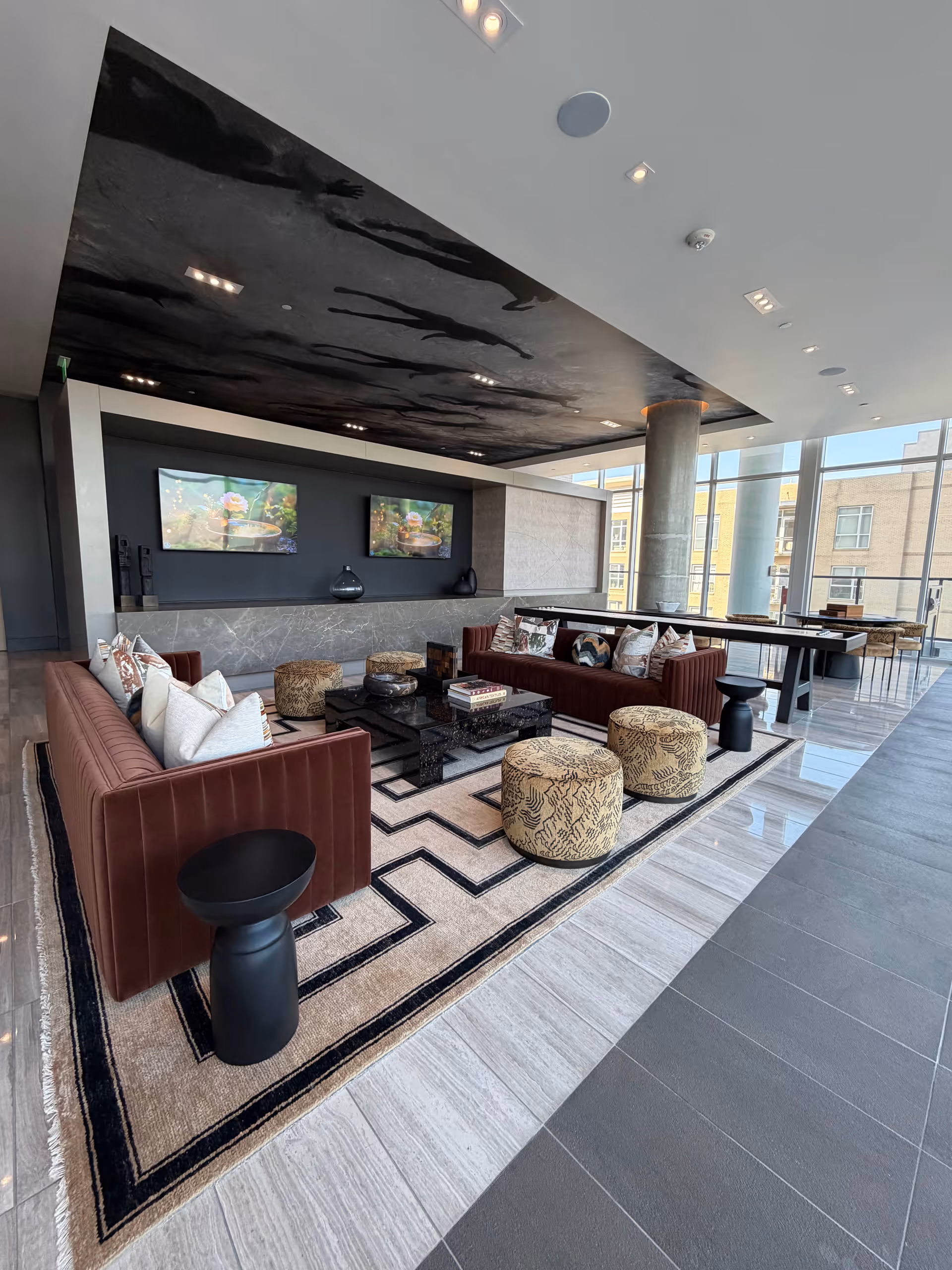 Spacious modern lounge with red sofas, ottomans, and a coffee table by large windows.