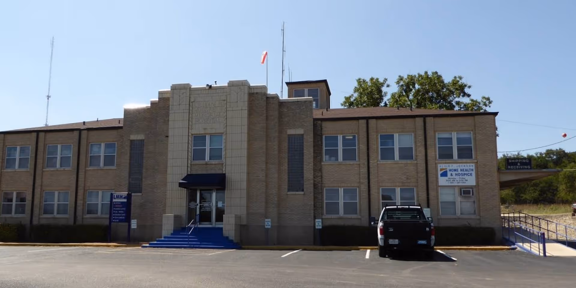 A brick senior living facility front with blue steps and a parked black pickup.