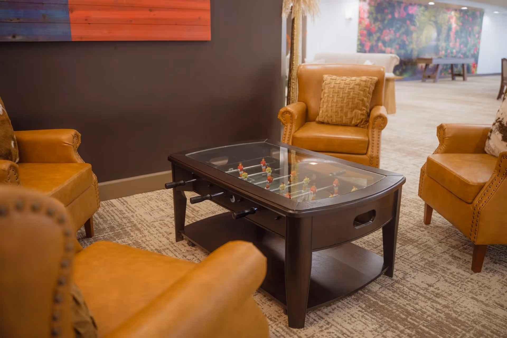 Leather armchairs surround a glass-topped foosball table in a cozy lounge.