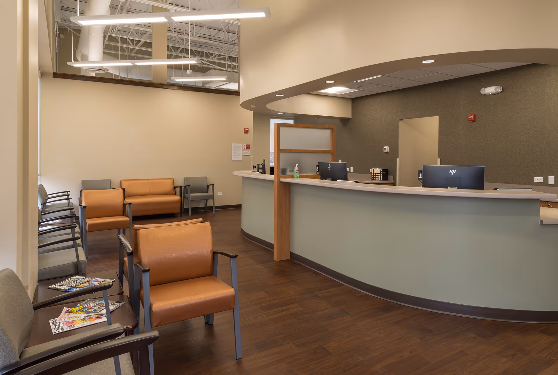 Reception area with curved front desk, wooden flooring, and waiting chairs inside a clinic.
