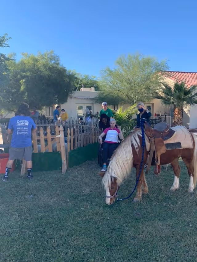 Residents and staff gather in a sunny outdoor yard with a pony nearby.