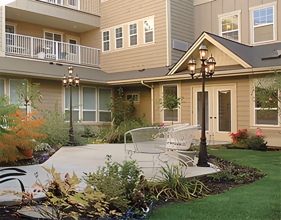 Outdoor courtyard of an assisted living building with benches, lamp posts, landscaping, and balconies.