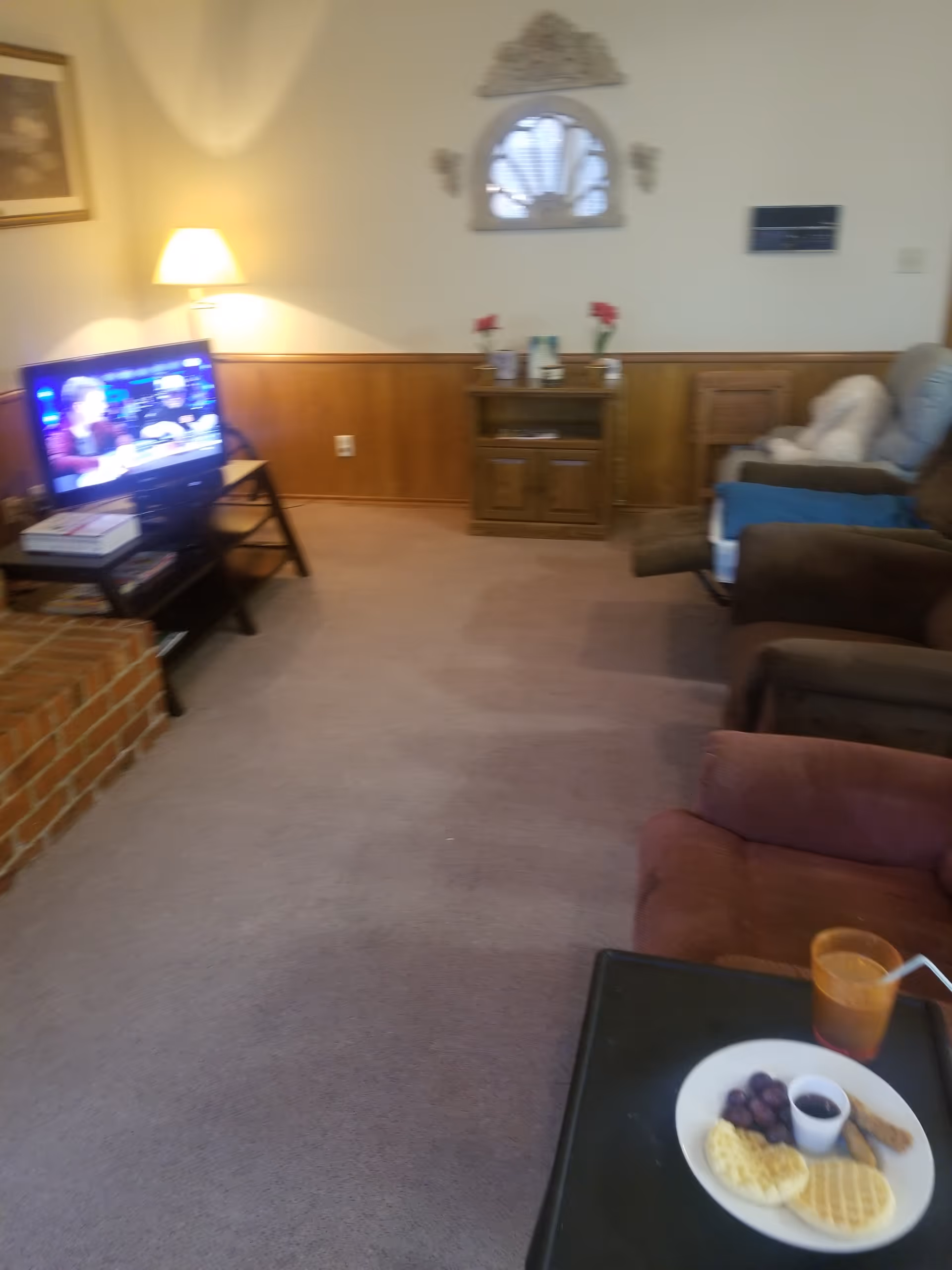 Cozy senior living living room with TV, recliners, wooden paneling, and a plate of breakfast items.
