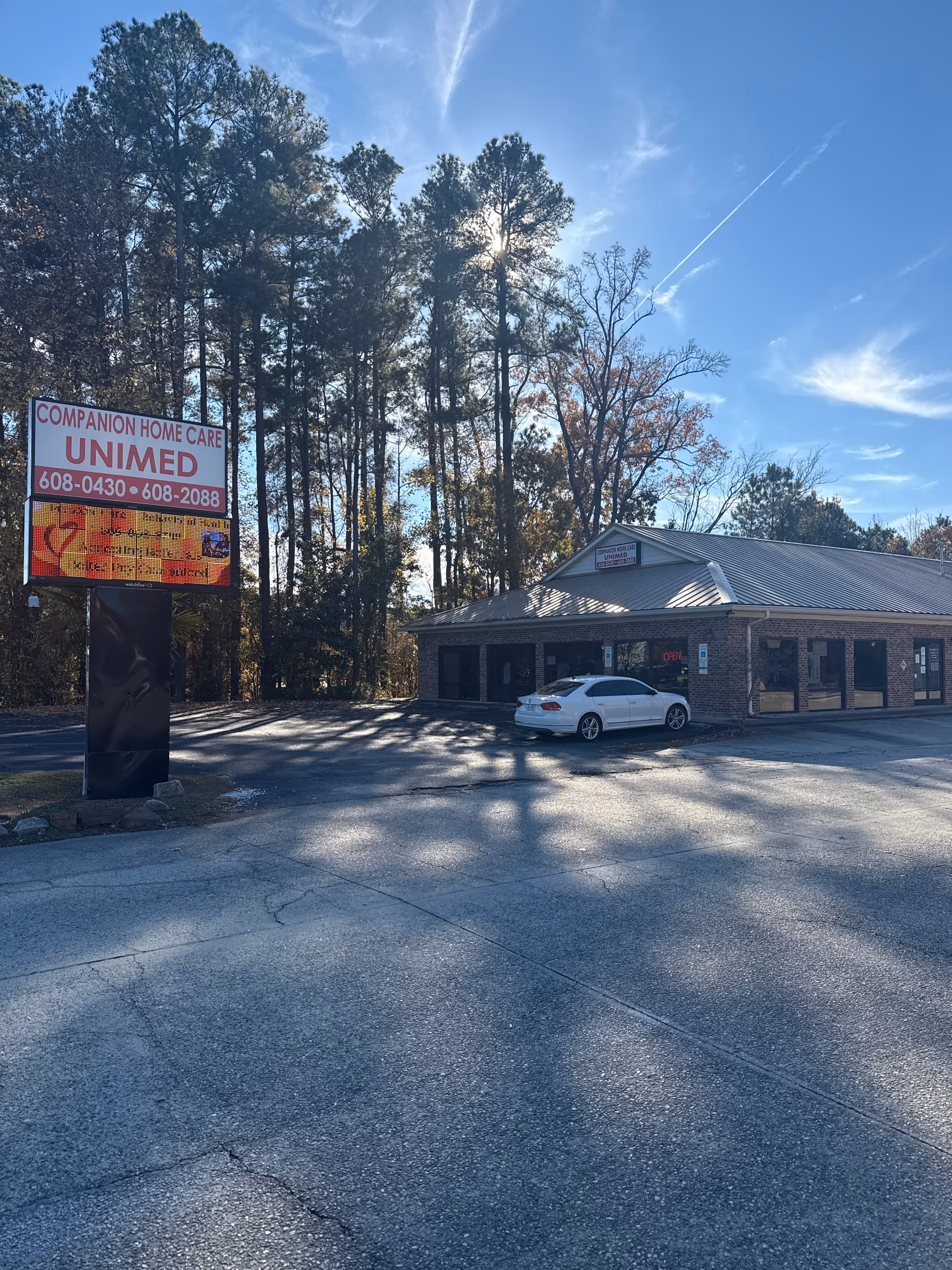 Exterior view of Companion Home Care building with a sign, trees, and a white car.